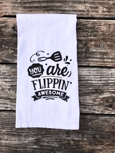A white cotton kitchen towel with black vinyl design of "you are flippin awesome" with a spatula.  A great kitchen gift!