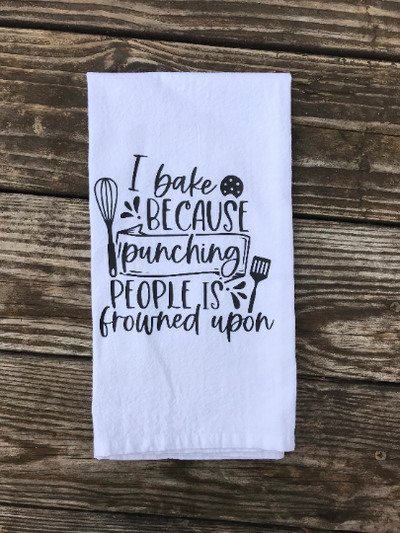 A white, cotton kitchen towel with black vinyl design that says "I bake because punching people is frowned upon".  A funny kitchen gift for bakers!