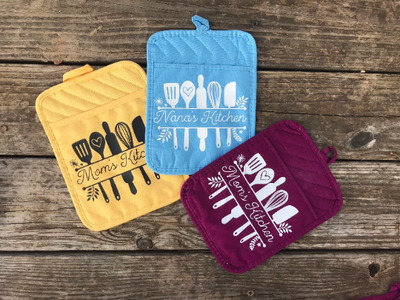 Cute pocket potholders with vinly design of cooking utensils with the quote "mom's kitchen" in between the utensils.  Available in yellow, light blue, and purple hot pads